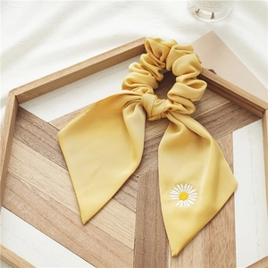Détail d'un chouchou en satin jaune avec broderie marguerite sur plateau bois