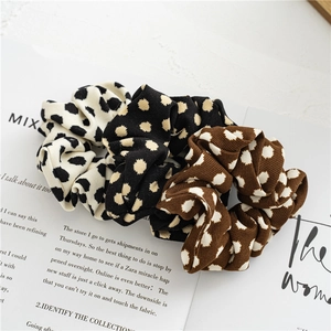 Detailed view of three spotted fabric scrunchies in cream, black, and brown colors