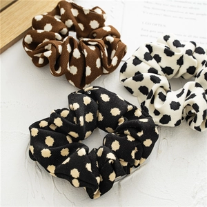 Close-up of three dotted scrunchies in brown, white and black with ribbed fabric texture