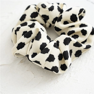 Polka dot fabric scrunchie in black and white knit material on minimalist stone background