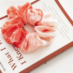 Dettaglio di scrunchie in chiffon tie-dye arancione e bianco con morbide pieghe