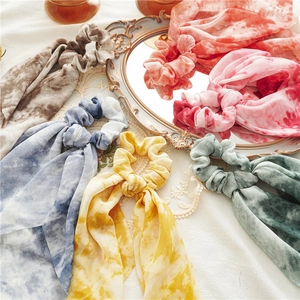 Detail view of colorful tie-dye silk scrunchies with long ribbons arranged on a vintage mirror