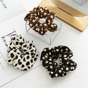 Three-piece polka dot fabric hair scrunchies in brown, cream, and black on a textured base