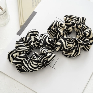 Detailed view of two zebra pattern scrunchies on white card with decorative props