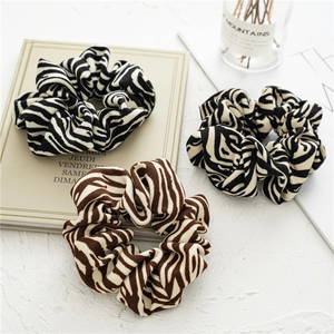 Detailed view of three zebra-patterned fabric scrunchies in black, cream, and brown tones