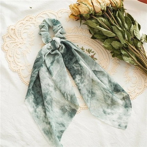 Close-up of a tie-dye dark green silk scrunchie with long ribbons on vintage lace
