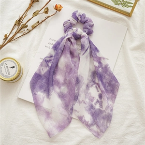 Detailed view of a purple and white tie-dye chiffon scrunchie with long ribbons on a magazine