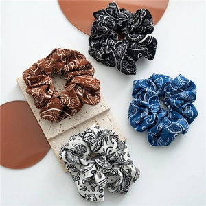 Close-up of four paisley print scrunchies in black blue brown and white fabric