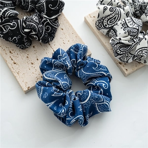 Three-piece paisley scrunchie set in black, white, and navy on a neutral stone display