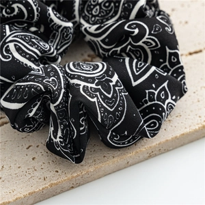 Detail of vintage black and white paisley scrunchie on textured beige stone surface
