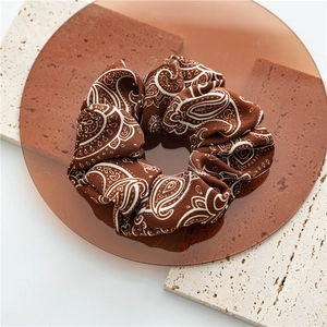 Detail of coffee brown paisley scrunchie with vintage pattern on textured stone