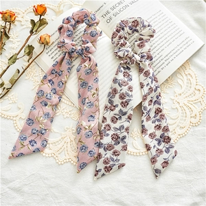 Close-up of two floral chiffon scrunchies with long streamers in pink and beige rose patterns