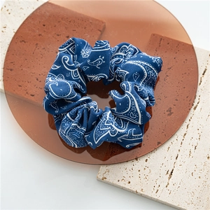 Detail of navy blue paisley hair scrunchie on amber display with stone background