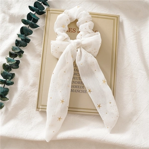 Detail von cremefarbenem Chiffon-Haargummi mit goldenen Sternen auf einem Buch