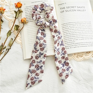 Detailed close-up of floral fabric hair scrunchie with ribbons on vintage book pages