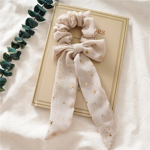 Detail eines cremefarbenen Chiffon-Haargummis mit goldenen Sternen und langen Bändern