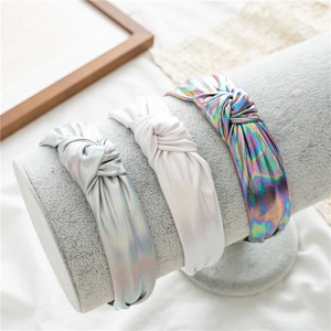 Three wide knotted headbands with metallic laser finish on a velvet display stand