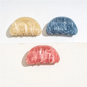 Close-up of three marble-textured acrylic hair claws in beige, blue, and coral pink