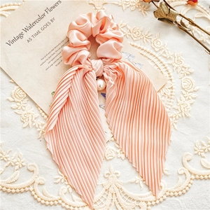Detailed close-up of pink satin scrunchie with long pleated ribbons and pearl pendant charm