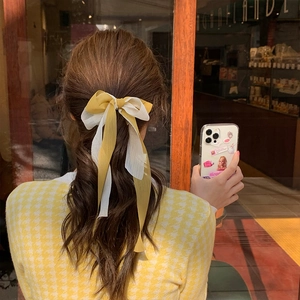 Détail d'un chouchou à nœud en mousseline jaune et beige porté en queue de cheval