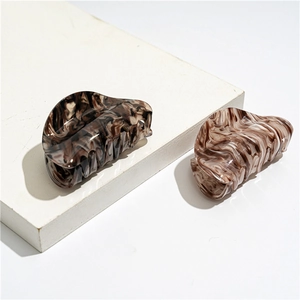 Detail of two large acrylic hair claws with marble and tortoiseshell patterns on white blocks