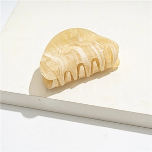 Macro shot of cream white acrylic hair claw clip with marble texture on stone block