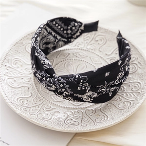 Détail d'un serre-tête torsadé à motif paisley noir et blanc sur une assiette ciselée
