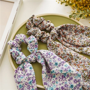 Détail de chouchous à fleurs avec longs rubans en violet et orange sur un plateau vert