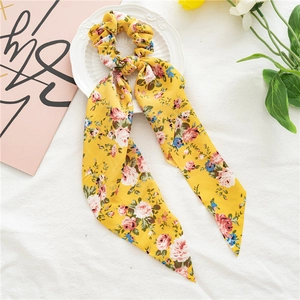 Détail d'un chouchou à fleurs jaunes avec de longs rubans posé sur une assiette blanche