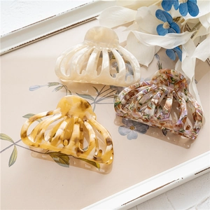 Three acetate hair claws in cream, amber, and marble patterns on a decorative tray