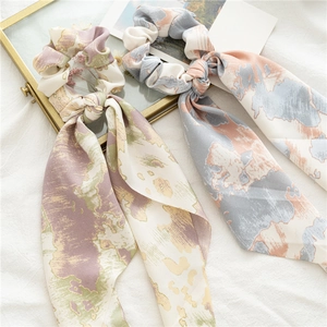 Détail de deux chouchous en satin tie-dye avec de longs rubans sur tissu blanc
