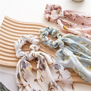 Florale Satin-Haargummis mit langen Bändern in Hellrosa und Blau auf Holztablett