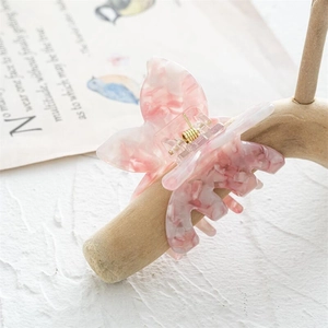Détail de la pince à cheveux papillon en acétate rose marbré avec ressort doré sur bois