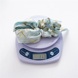 Hellblauer Haargummi aus Satin mit Blumenmuster und langen Bändern auf einer Digitalwaage