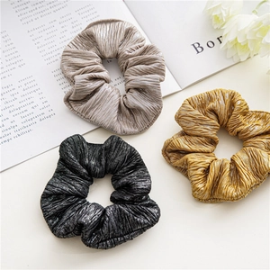 Trois chouchous plissés en satin champagne, noir et jaune posés sur un bureau blanc