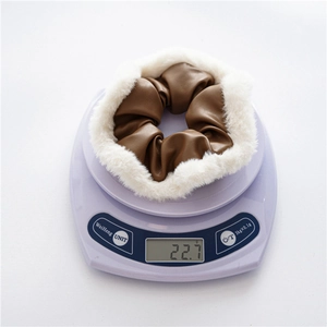 Close-up of brown PU leather scrunchie with white faux fur trim on a purple scale