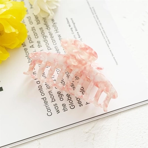 Close-up of pink marble pattern acetate hair claw clip with interlocking teeth on a magazine
