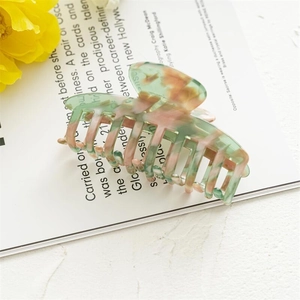 Detail view of large marble texture hair claw clip in pastel green and pink on a magazine