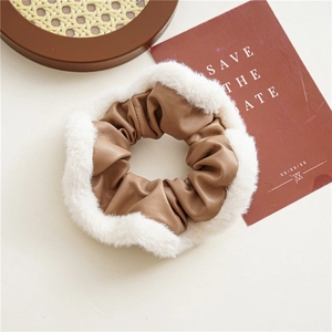 Close-up of brown PU leather scrunchie with white plush trim on a beige desk