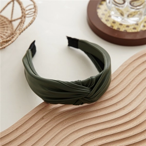 Dettaglio del cerchietto in pelle PU verde scuro con texture a nodo su legno
