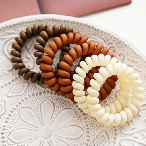Close-up of matte spiral hair ties in earth tones on a white embossed ceramic plate