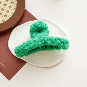 Gros plan d'une pince à cheveux en peluche verte avec texture douce sur plateau déco