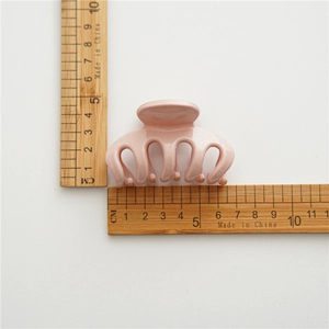 Detail view of a pale pink hair claw clip showing size dimensions with a ruler