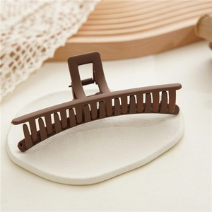 Close-up of a matte dark brown shark hair claw clip with a square handle on wood texture