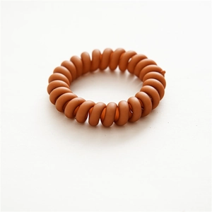Detailed top view of a matte dark brown spiral telephone wire hair tie on a white surface