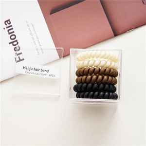 Detail of six high-elasticity spiral hair ties in a clear storage box with neutral colors
