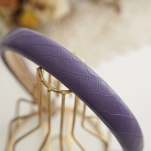Close-up of dark purple snake skin embossed PU leather headband on a gold stand