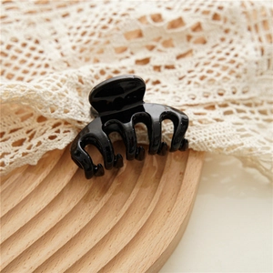 Glossy black shark hair claw clip on decorative wood tray with lace background detail