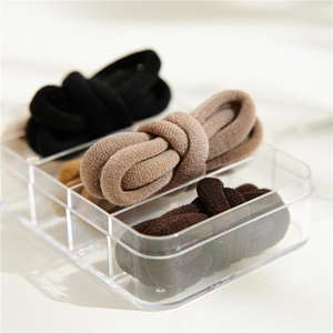 Detail of thick elastic hair ties in neutral earth tones stored in a clear acrylic box