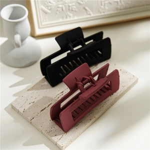 Détail de grandes pinces à cheveux rectangulaires noir mat et bordeaux sur pierre